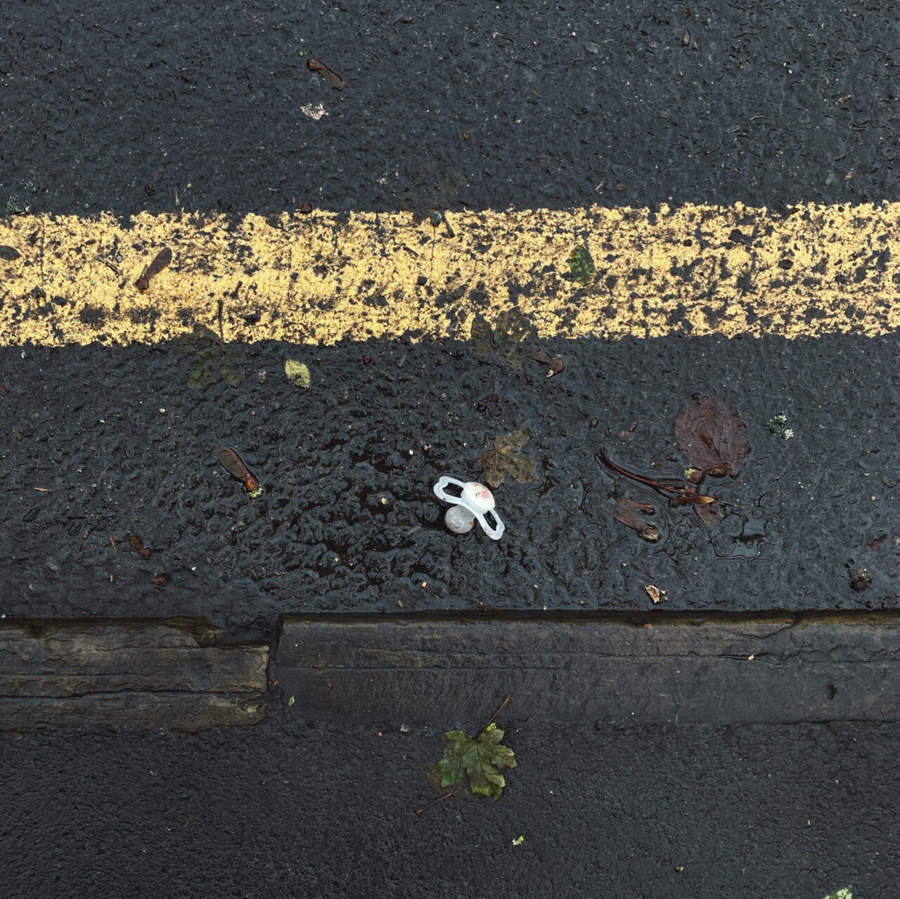 Photograph looking down at a dummy in a gutter by the side of the road, with pavement at the bottom and single yellow line above.