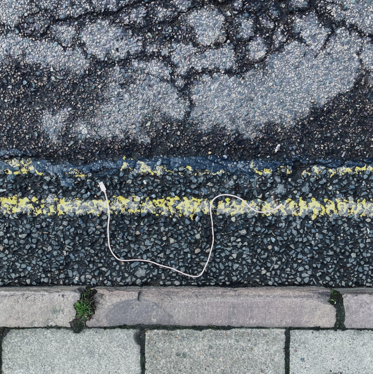 Photograph looking down at a USB cable in a gutter by the side of the road, with pavement at the bottom and double yellow lines above.