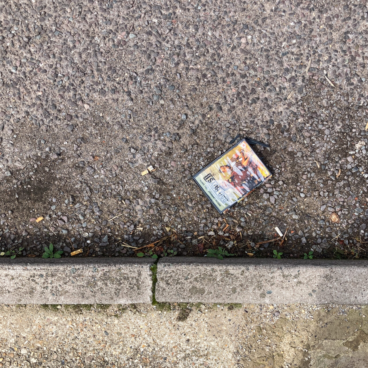 Photograph looking down at the gutter at the side of the road with the curb at the bottom of the frame and a DVD of 'Bad Boys II' in the centre of the frame