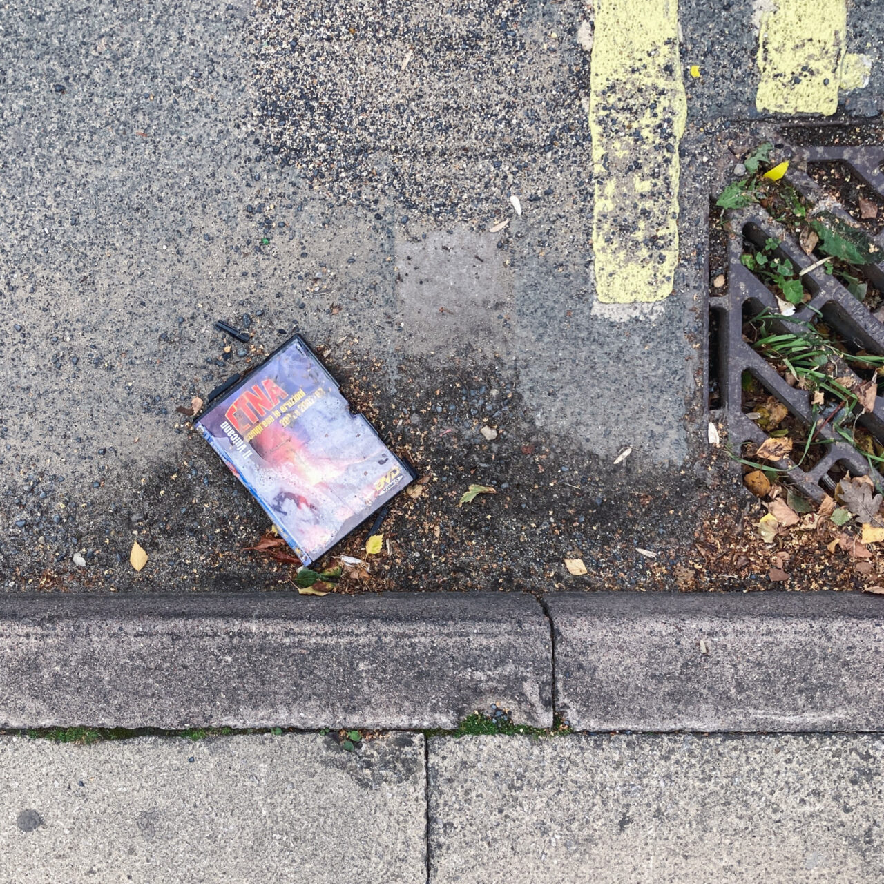 Photograph looking down at the gutter at the side of the road with the curb at the bottom of the frame, a painted yellow line at the top right of the frame and a DVD copy of 'ETNA' in the centre of the frame.