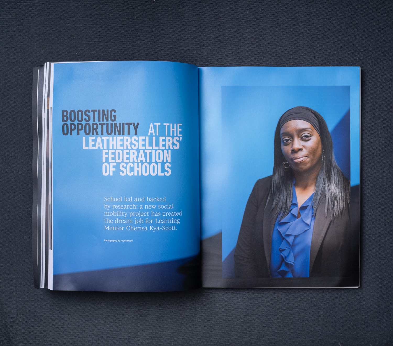 The Leathersellers' Review. Photograph of the The Leathersellers' Review publication open on a page with a portrait of Cherisa Kya-Scott on the right and 'boosting opportunity at the Leathersellers' Federation of Schools' on the left, photographed on a dark grey background.